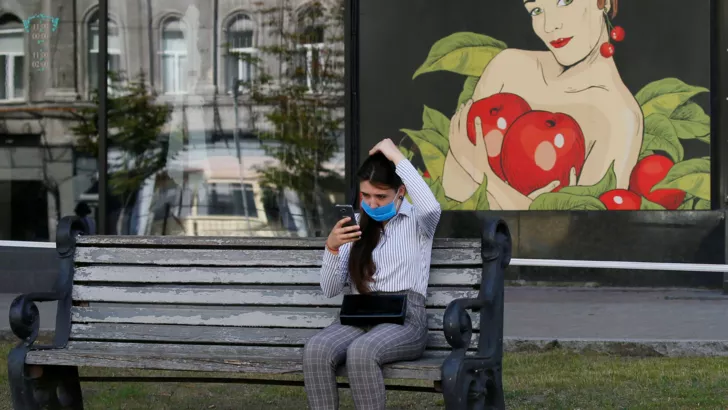 Девушка в маске сидит на лавочке в Киеве.