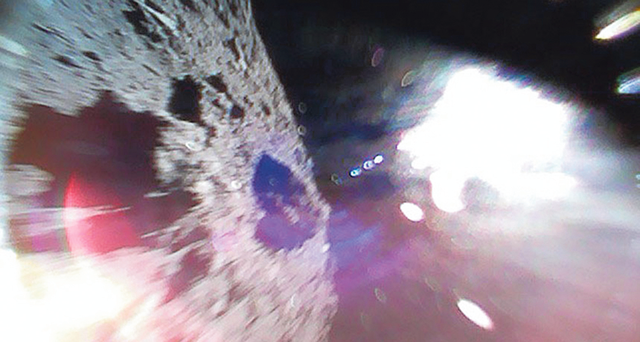 Посадка. Фото, сделанное в ходе спуска роботов на Рюгу (слева — поверхность астероида, белое пятно справа — Солнце). Фото: JAXA