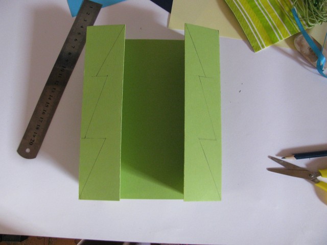 2. Далее сгибаем картон по образованным нажатием ножниц линиям два раза с каждой стороны — сперва внутрь, затем наружу — так, как это показано на фото справа. На тех сторонах, которые получились верхними, рисуем простым карандашом елочку.
