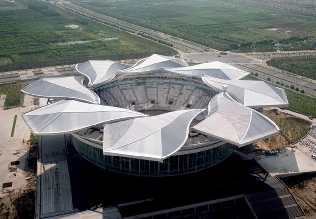 8. Стадион Qi Zhong<br />
Стадион Qi Zhong  в Шанхае является вторым по величине теннисным центром в Азии. Его площадь составляет почти 340 тысяч квадратных метров. Стадион вмещает до 15 тысячи зрителей и имеет более 900 парковочных мест. Центральный теннисный корт занимает более 30 тысяч квадратных метров. Крыша стадиона состоит из восьми частей похожих на лепестки магнолии – цветка Шанхая, каждая из которых весит по две тонны. Благодаря такой конструкции на стадионе проводятся теннисные турниры как на открытой местности, так и под крышей.<br />
