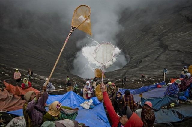 Местные сельские жители ловят дары, которые к вулканам приносят верующие индусы, 24 июля.