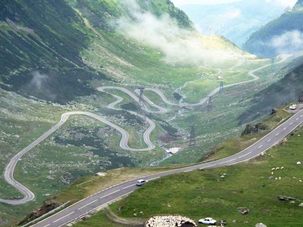 Трансфэгэрашское шоссе, Румуния<br />
Трансфэгэрашское шоссе — горное шоссе в Карпатах, соединяющее румынские области Валахию и Трансильванию и проходящее через горный массив Фэгэраш. Наивысшей точки достигает на высоте 2034 метра и является самой высотной дорогой Румынии. Шоссе было построено в 1970—1974 годах по приказу Николае Чаушеску для военных нужд. Как и многие другие масштабные проекты, строительство Трансфэгэрашского шоссе потребовало огромных затрат: только динамита было потрачено порядка 6000 тонн. Не обошлось и без жертв — на строительстве дороги погибли около 40 человек. Сегодня это шоссе считается одной из красивейших дорог в мире и является одной из достопримечательностей Румынии. В его окрестностях также находятся и другие румынские достопримечательности: горное озеро и водопад Быля и крепость Поенари а также известная как резиденция Влада Дракулы. Сквозное движение по дороге между северными и южными склонами Карпат открыто только в июле и августе, и только в светлое время суток. В 2009 году на этой дороге тестировали свои спорт кары ведущие Top Gear, и Джереми Кларксон назвал ее лучшей для езды на спортивных машинах.<br />
