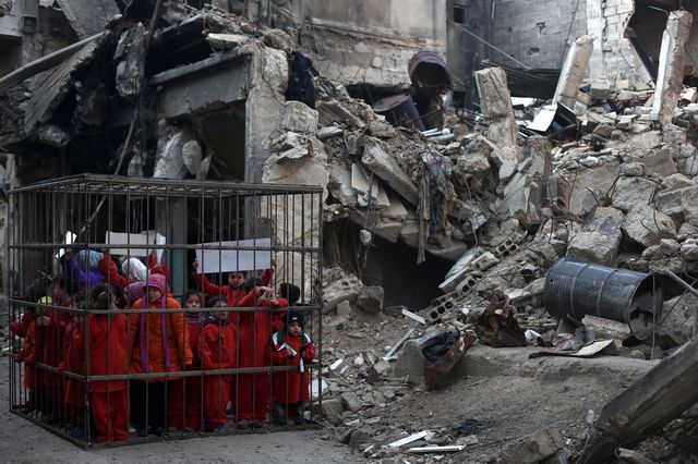 В сирийском городе Дамаск детей посадили в клетку рядом с разрушенным зданием после бомбежки.  Такой акцией протеста люди просят осудить продолжающееся убийство мирных жителей. Фото: AFP