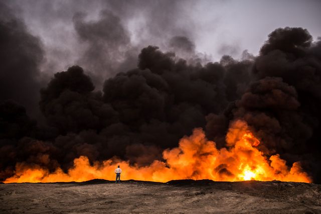 19 октября, 2016 года. Мужчина стоит перед огнем из масла, которое было подожжено примерно в 60 км к югу от Мосула в ходе операции иракских сил против Исламского государства. Фото: AFP